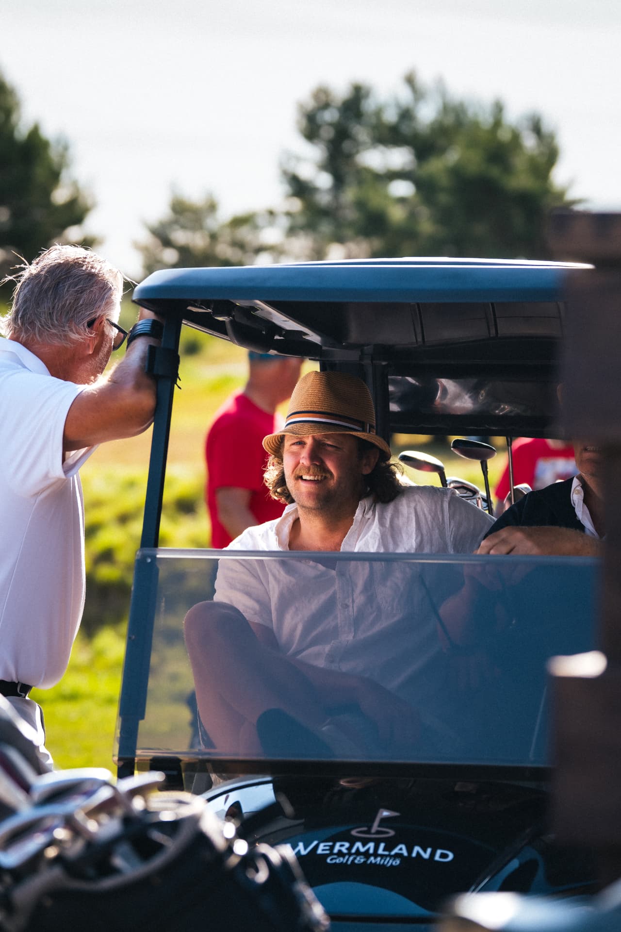 Deltagare i hatt sitter i golfbilen och skrattar