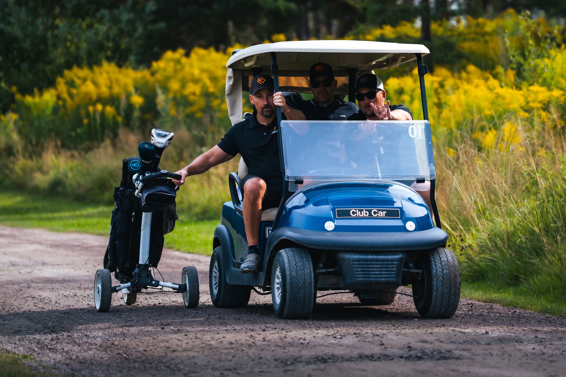 Golfbil med tre spelare på väg längs banvägen