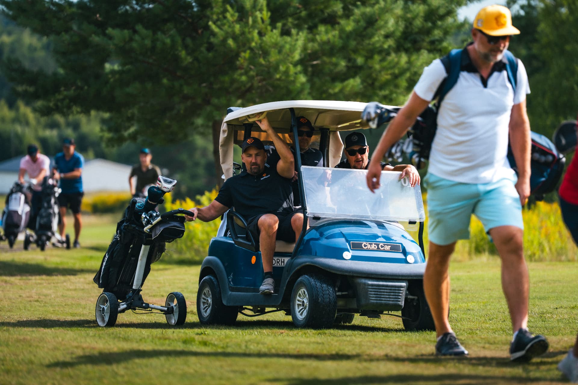 Golfbil och spelare i eftermiddagsljus på banan